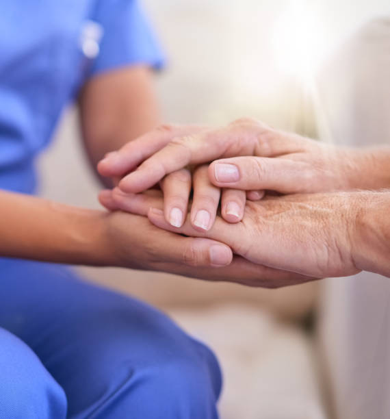 cropped shot of a nurse holding a senior woman's hands in comfort